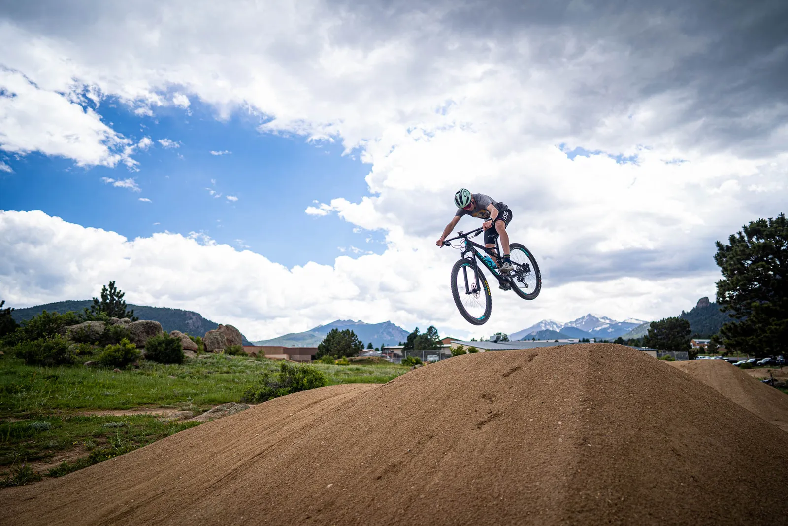 A mountain biker jumping over a dirt feature with Estes Park mountains in the distance